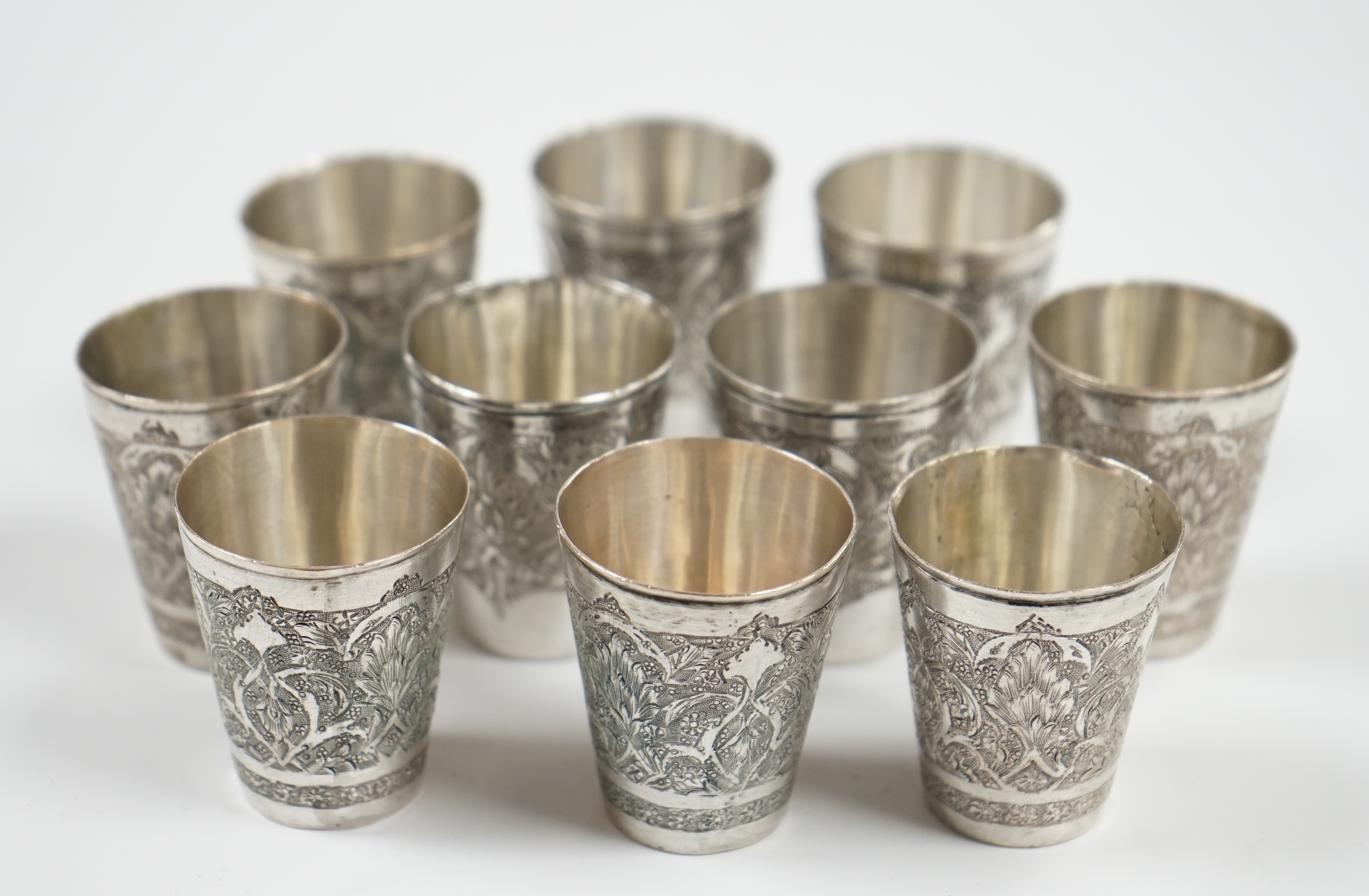 A set of four Persian engraved white metal tot cups, 43mm, stamped marks to the base and six other similar tot cups, 44mm, 8.7oz. Condition - fair